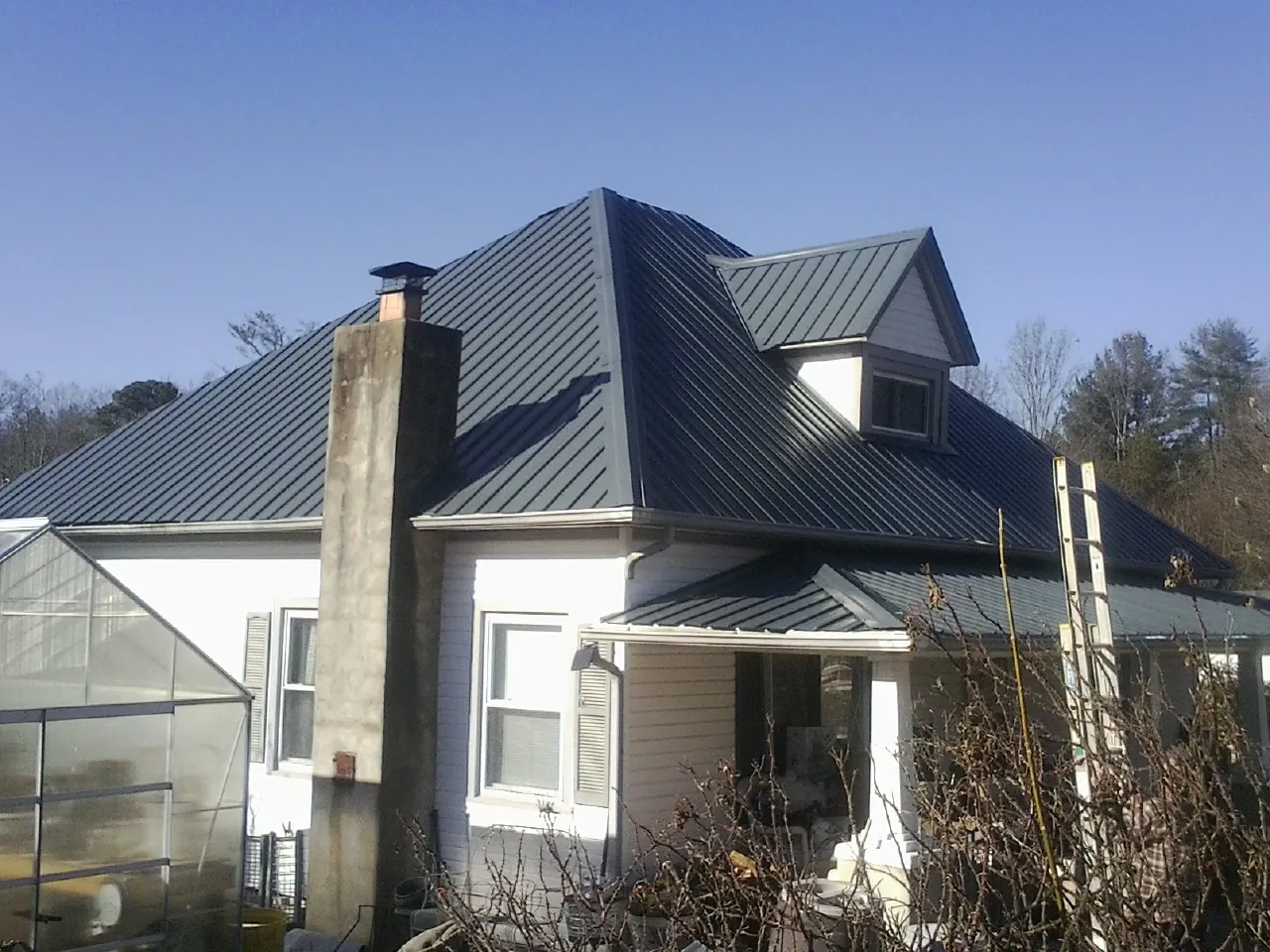 Dark blue standing seam metal roof on a white farmhouse with dormer — Slate & Tile Roof Repair by Roofing Brothers in Heflin