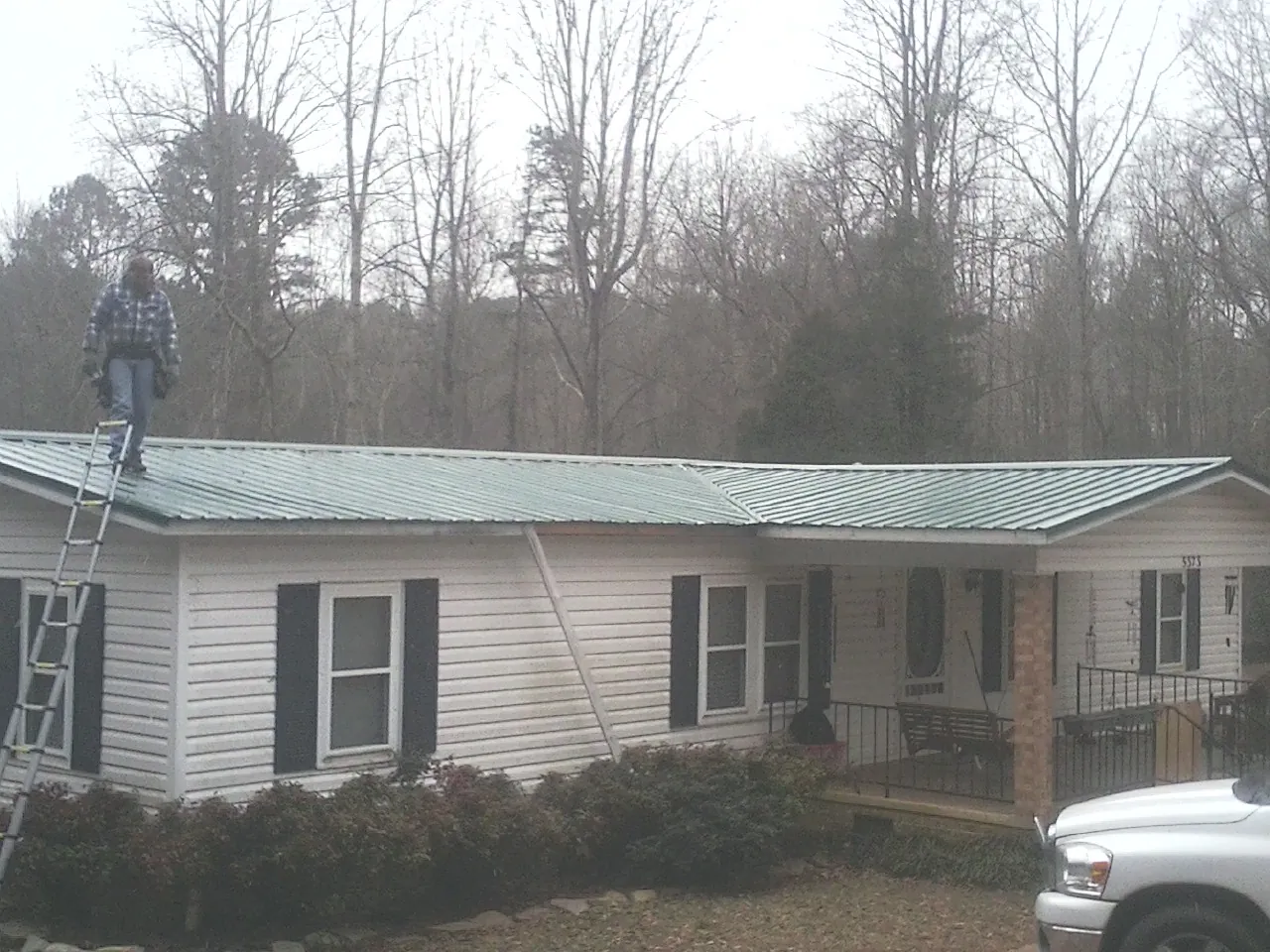 Worker on a ladder beside a new green metal roof on a ranch home in Heflin