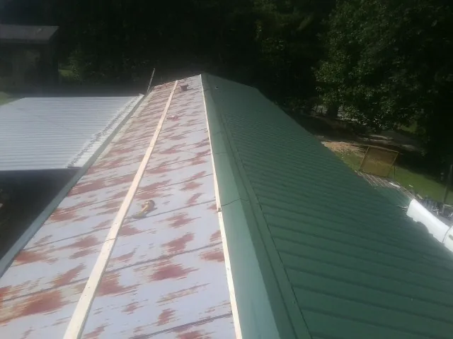 Old rusted panels beside newly installed green metal roofing — Wind Damage Roof Repair by Roofing Brothers in Heflin