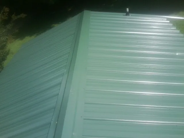 New green metal panels meeting at the ridge of a roof — Flat Roof Repair work by our crew in Heflin