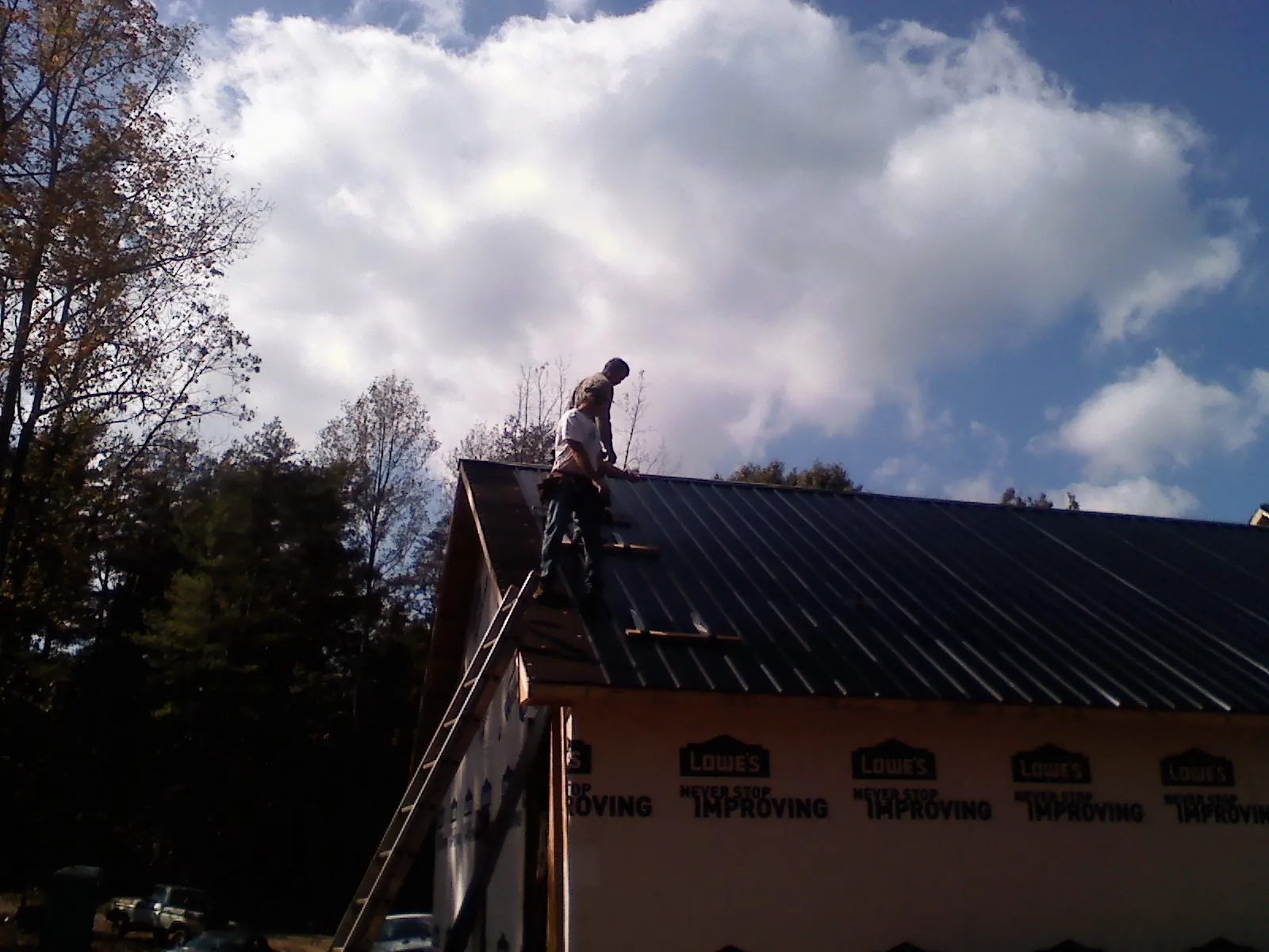 Roofer fastening dark metal panels high against a cloudy sky, from a Roof Inspection job in Heflin