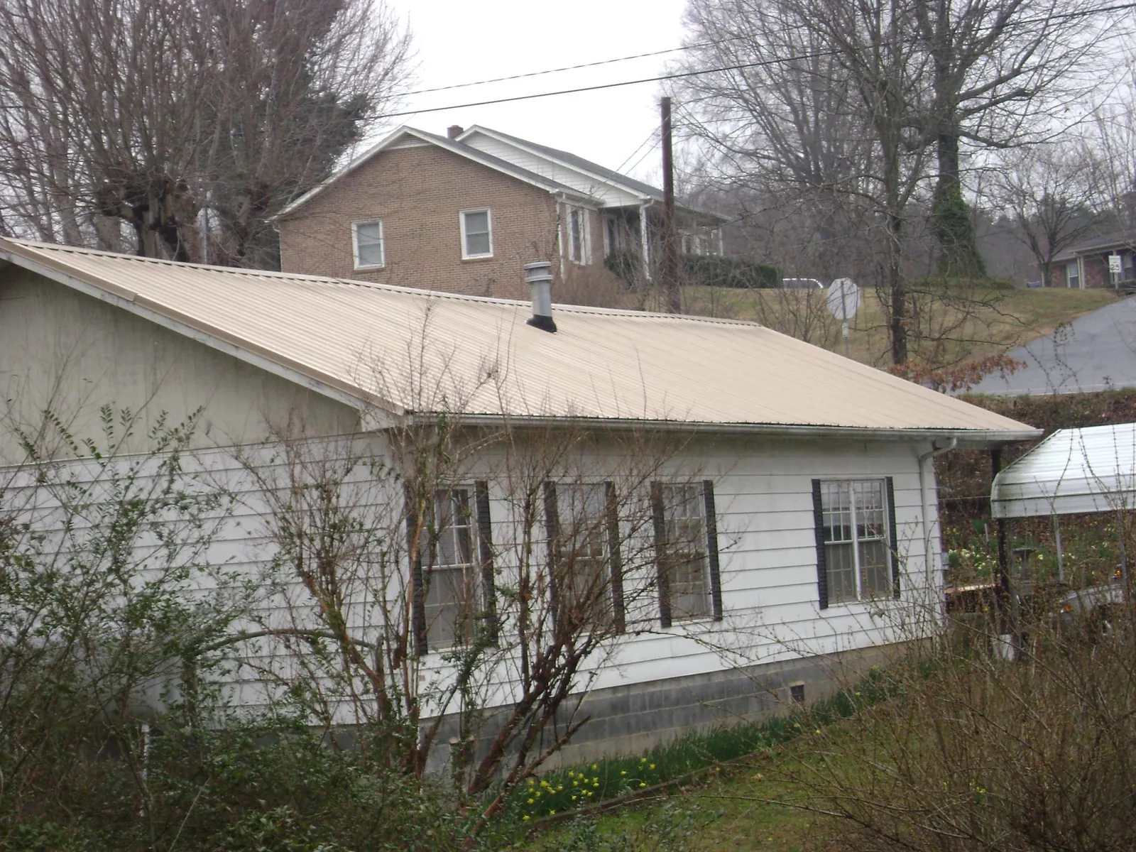 Tan metal roof on a white sided house set into a hillside — Commercial Roofing by Roofing Brothers in Heflin