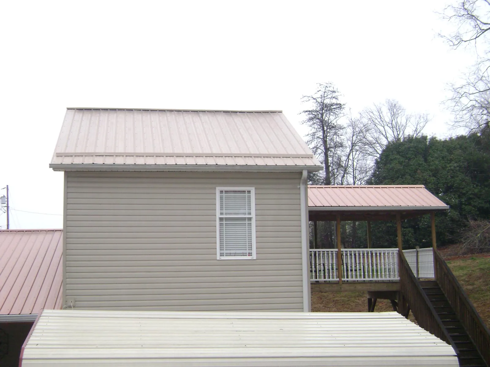 Tan metal roofs on a two story addition and attached porch, from a Roof Replacement job in Heflin